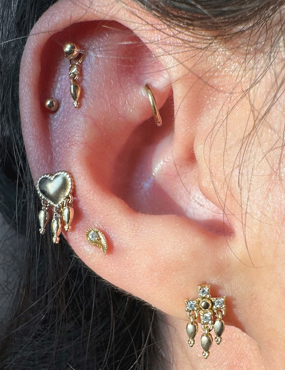 14k gold piercing studs with tassels and diamonds by honey drip placed on the ear lobe and helix.
