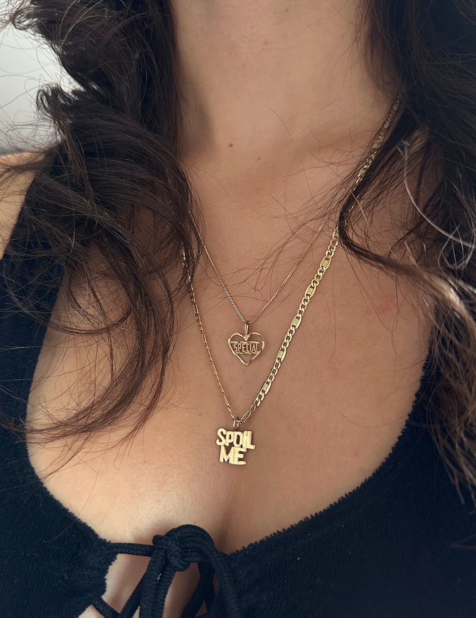 Person wearing a set of vintage 14k yellow gold charm necklaces that read "Spoil Me" and "Special" sourced by HONEY DRIP NYC